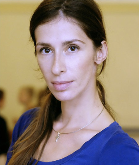 Natiya Kezevadze, long haired woman in a blue top in front of a yellow wall.