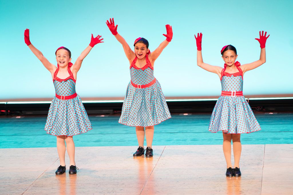 Steps Academy students in dance performance - three on stage in costumes with red gloved hands raised high