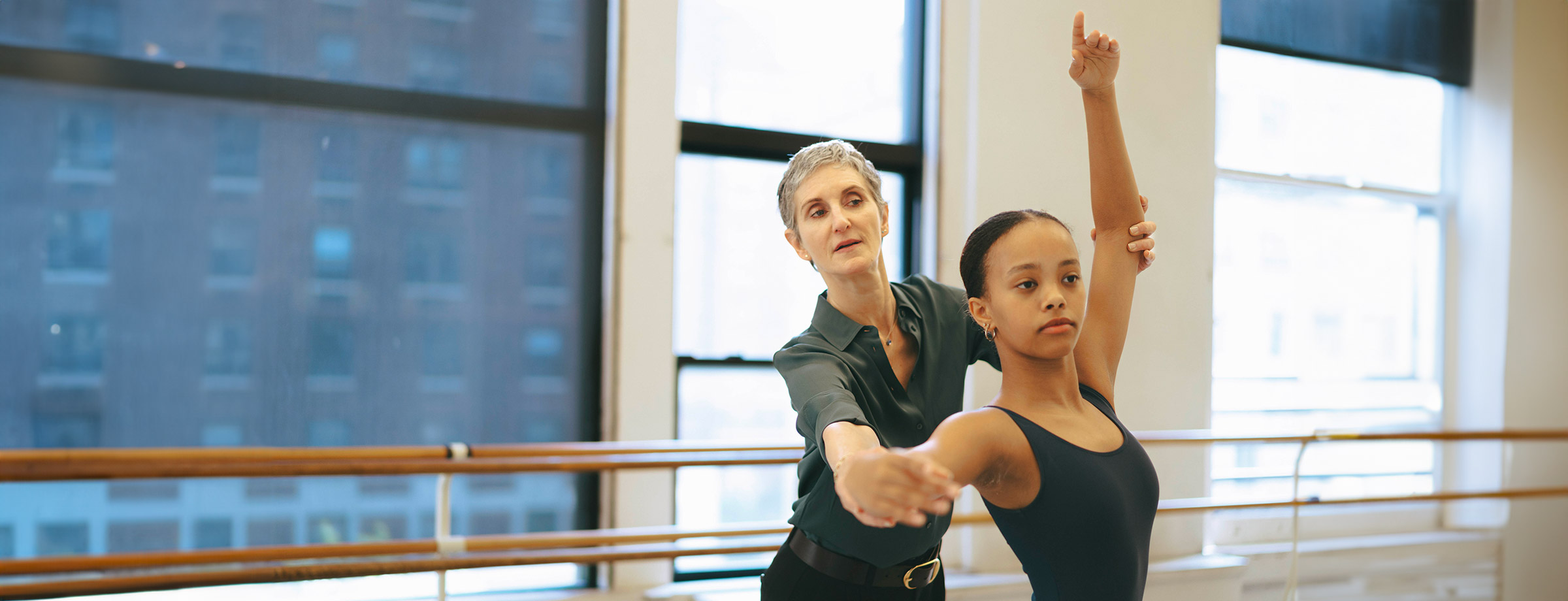 Jen Kreichman, director of the Steps on Broadway Academy is assisting an academy dancer in Steps dance studios - New York City visible through the windows above the barre